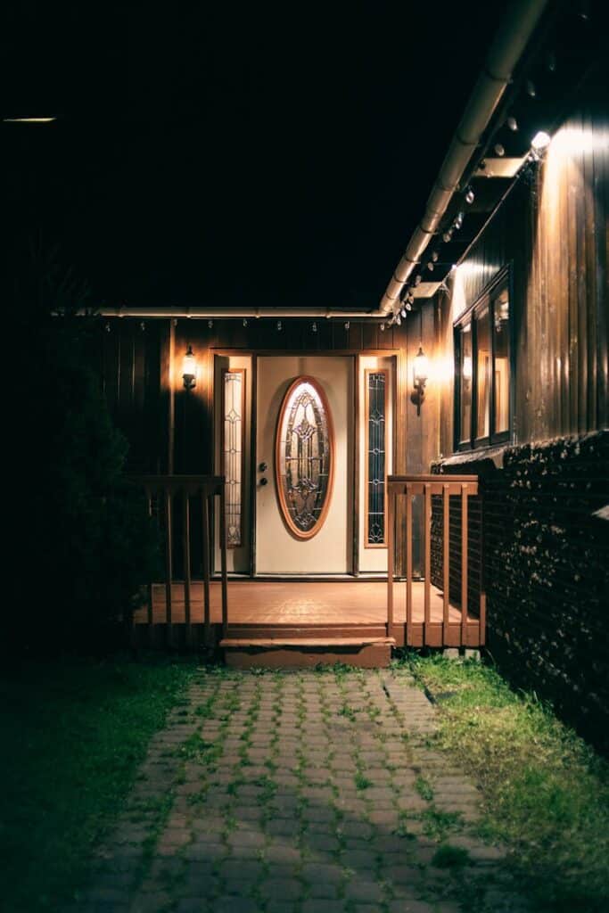 Warmly lit entrance of a house at night, featuring an inviting door surrounded by stylish windows.